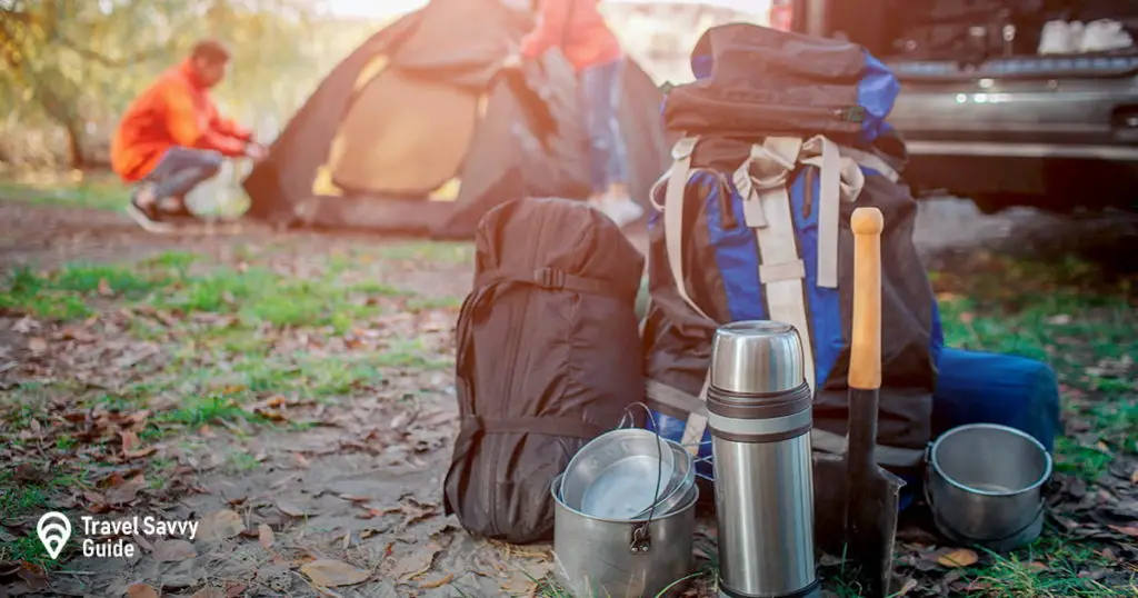 Picture of different expedition equipment. there are backpack with carimate, sleeping bag and dishes. young man and woman are packing tent. they are at car