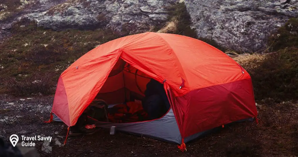 Red tent stands on the ground somewhere in the mountains