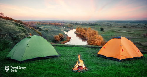 Camping from orange and green tents with fire on banks of river