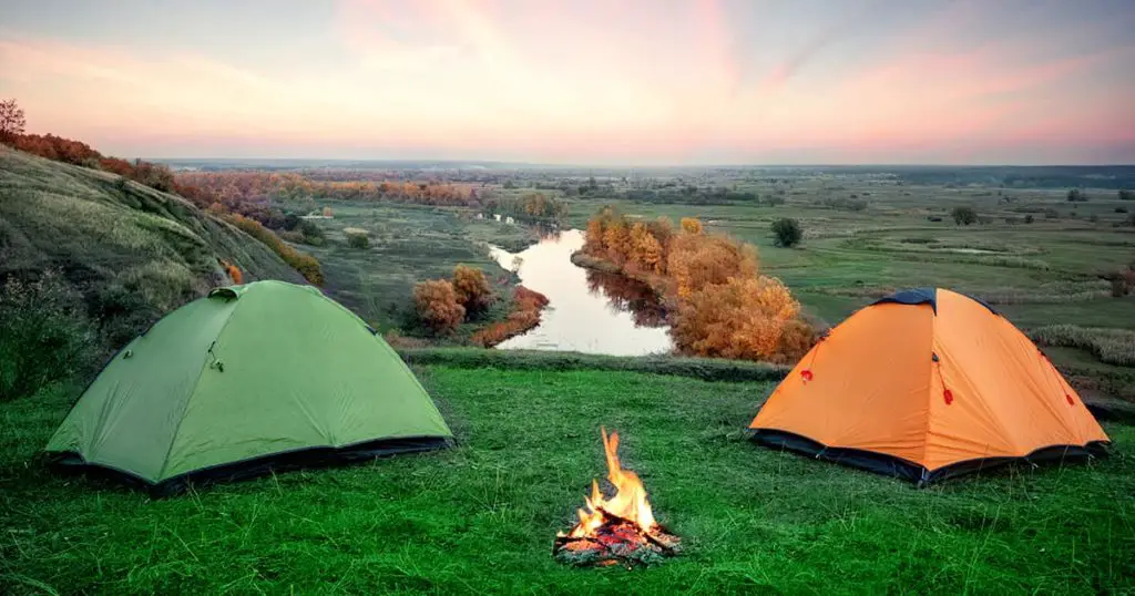 Camping from orange and green tents on banks of river