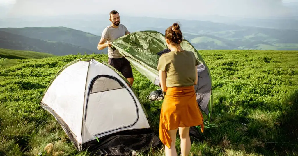 Young couple setting up the tent on the green meadow