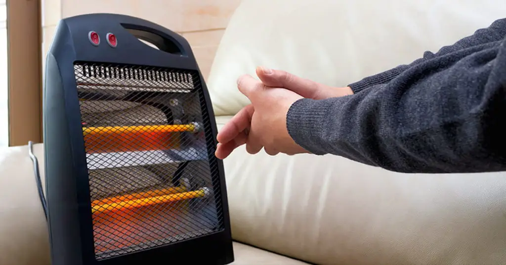 man sitting on sofa with an electric heater near his hands
