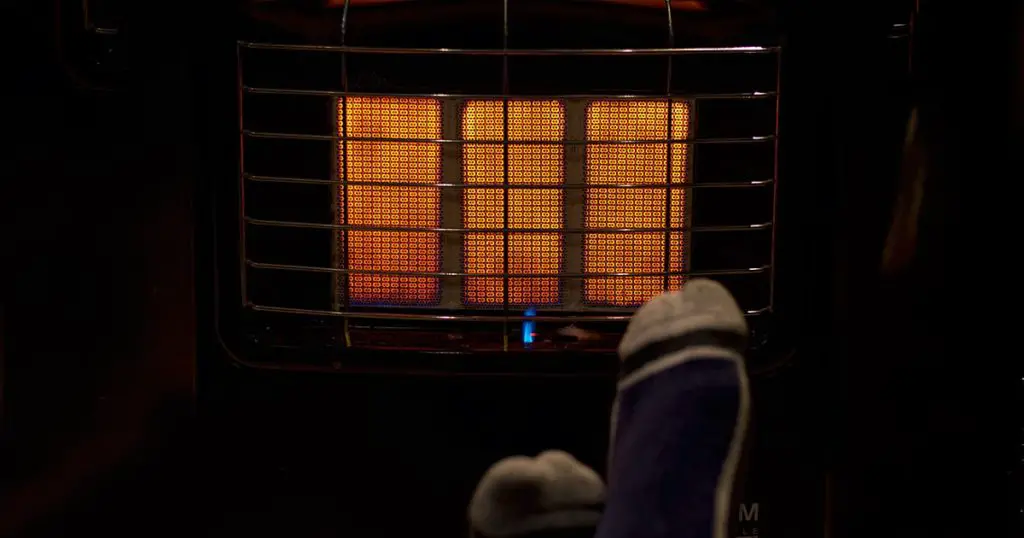 A photo of feet with socks getting some heat from a gas heater on a cold winter night.
