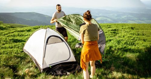 Young couple setting up the tent on the green meadow