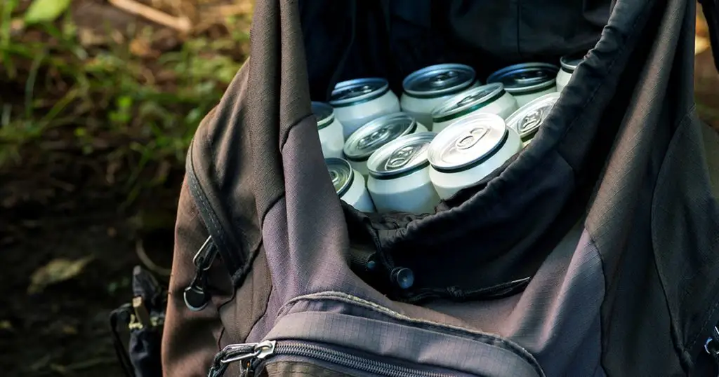 Beer in closed aluminum cans in a black tourist backpack on a natural background