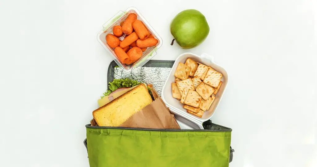 top view of sandwich and carrots with apple in lunch bag isolated on white