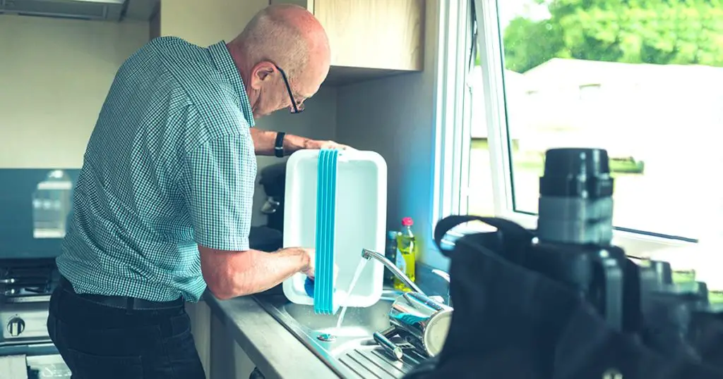 A senior man in a caravan is cleaning is cooler box