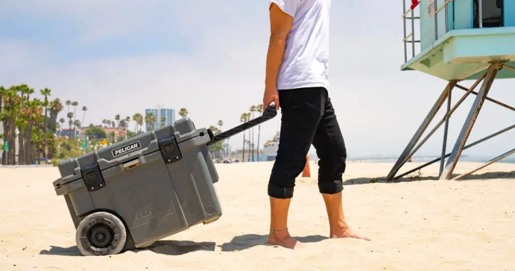 Man carrying a Pelican wheeled hard cooler on the beach