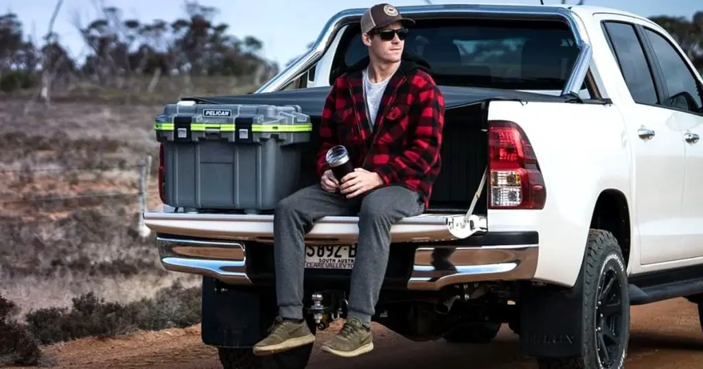 Man sitting in the back of a pickup near a Pelican hard cooler