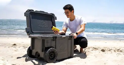 Man picking a beer from a Pelican wheeled hard cooler on the beach