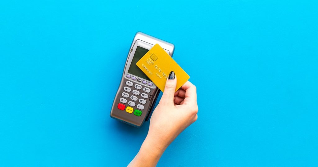 Woman's hand hold credit card, bring card to terminal on blue background top view copy space