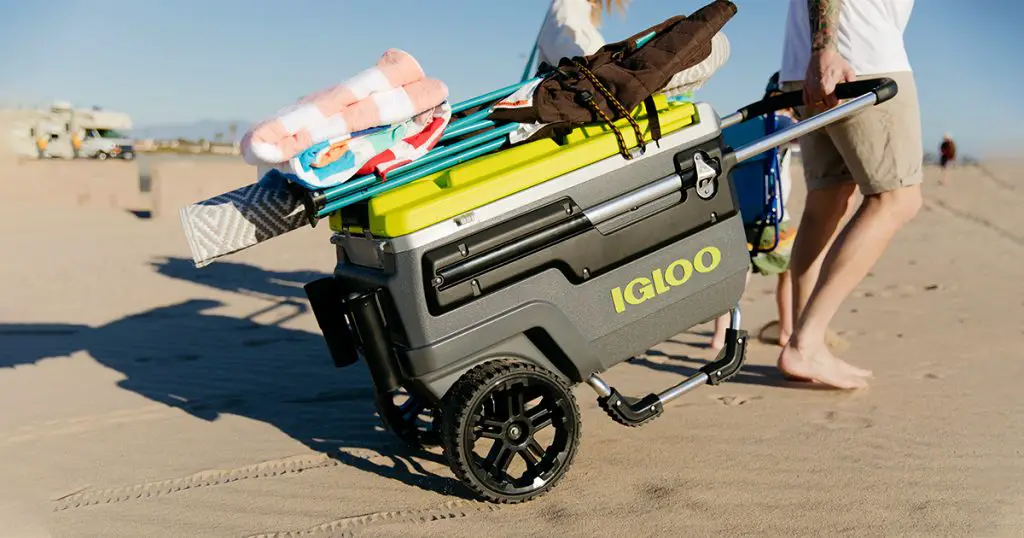 Man carrying igloo wheeled cooler on the beach