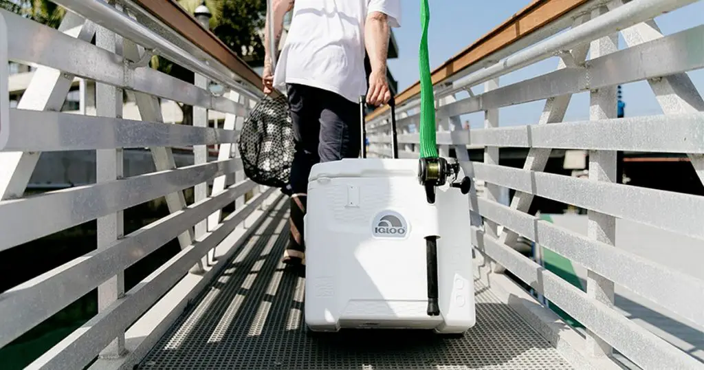Man carrying a Igloo Marine hard cooler with wheels