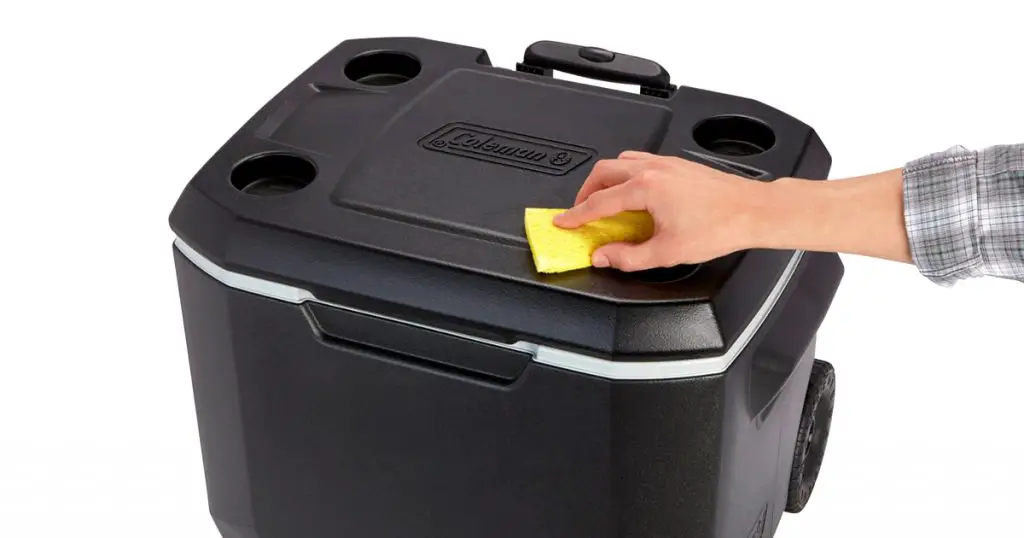 Man cleaning the top of Coleman hard cooler with wheels