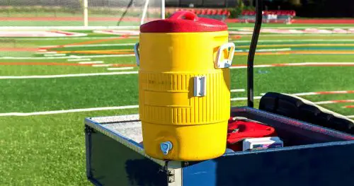 A yellow water cooler sits on a blue golf cart during a soccer game