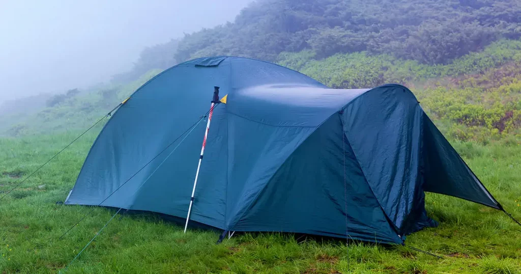 tent after the storm with ajar entrance mounted on the mountain meadow in a heavy fog