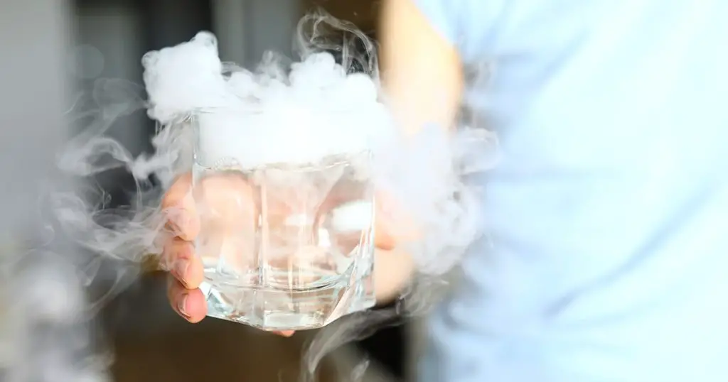 Close-up of person holding glass with water and cubes of dry ice