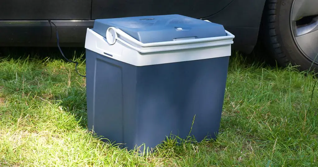 An electric fridge for a car on the grass, next to an electric car on a camping place