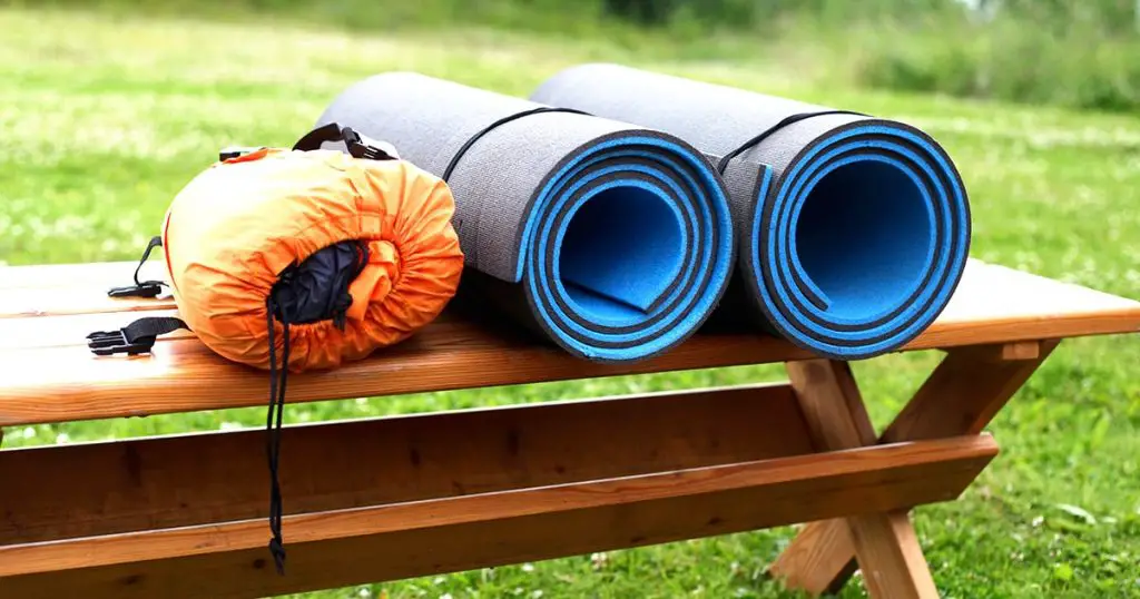 Sleeping pad and tent lie on a wooden bench.