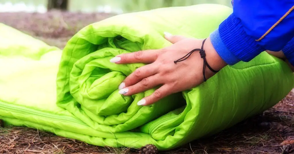 A woman folds and packs a sleeping bag, going on a journey through the forest.