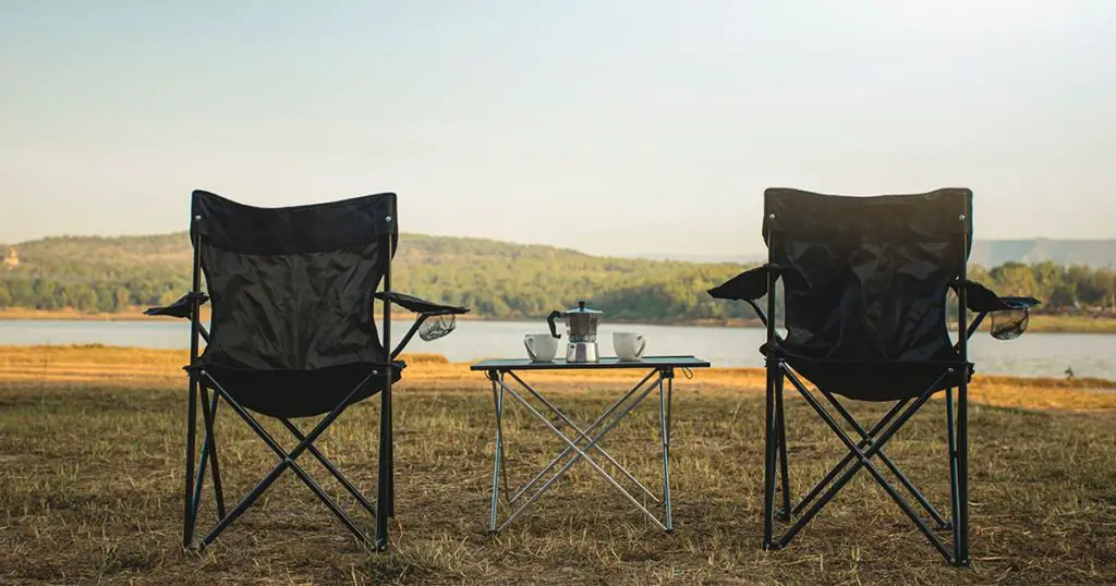 Outdoor two empty chairs with picnic table and moka pot coffee for Camping.