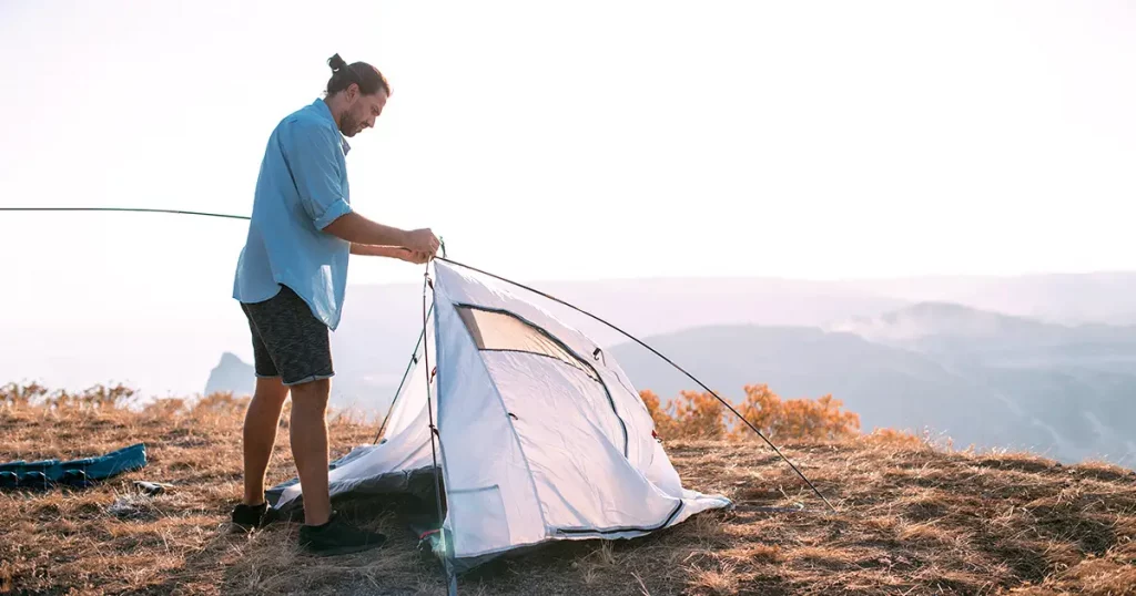 Young male tourist puts a tent in the mountains