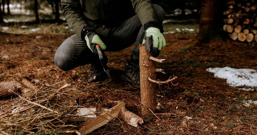 Man strong hands in gloves chop firewood with axe for bonfire