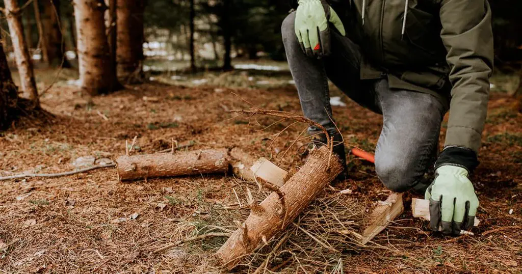 Man strong hands in gloves chop firewood with axe for bonfire