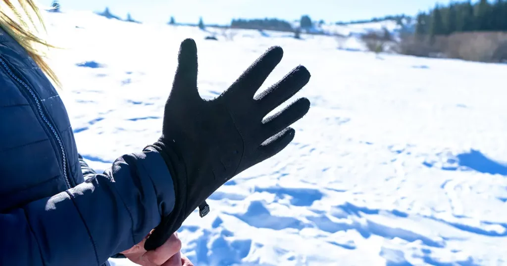 Woman putting winter sport glove in hand, getting ready for extreme cold weather and adventure activity.