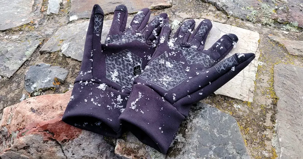 A pair of black gloves laying on brick wall with snow falling and trees in the background