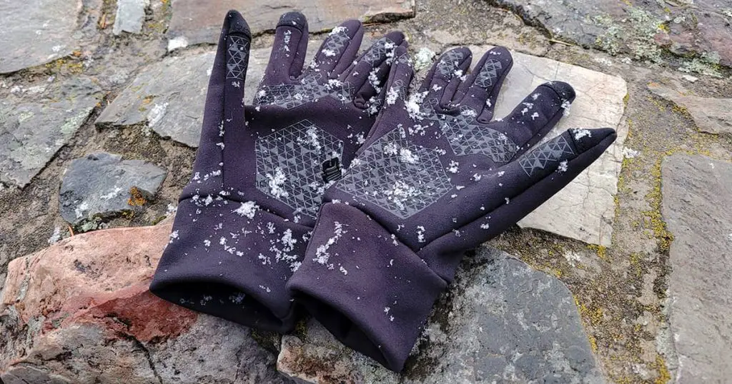 A pair of black gloves laying on brick wall with snow falling and trees in the background
