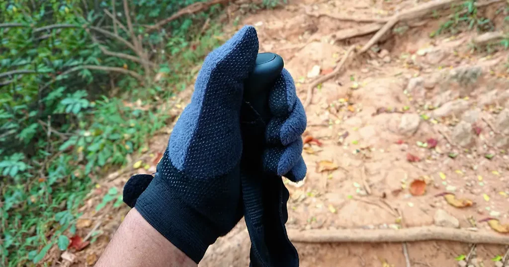 hand with glove catch the trekking pole on walk way in deep forest