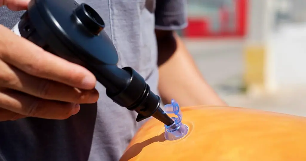 man nflating a pool air mattress with a hand held electric pump