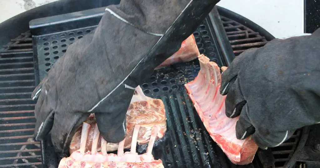 Man in large protective gloves cooking four large trimmed racks of ribs
