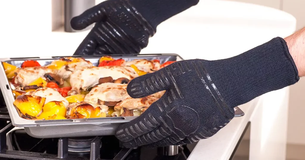 cook removes the hot tray from the oven in protective gloves