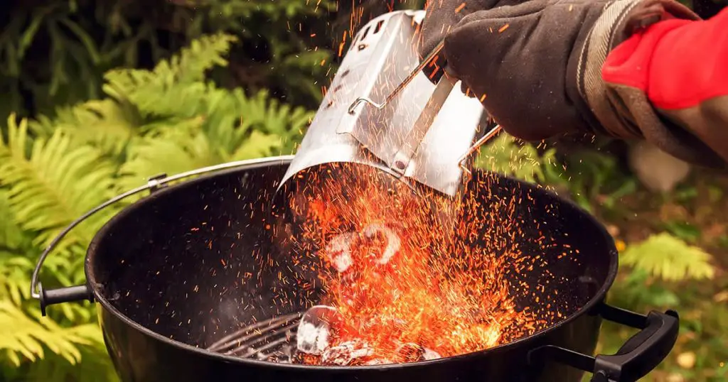 Close up man with gloves chimney starter barbecue grill in open air at country garden house