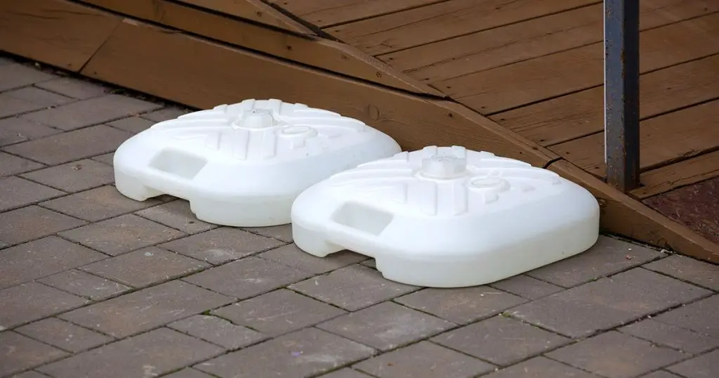 two plastic white bases of the beach umbrella stand are lying on the road