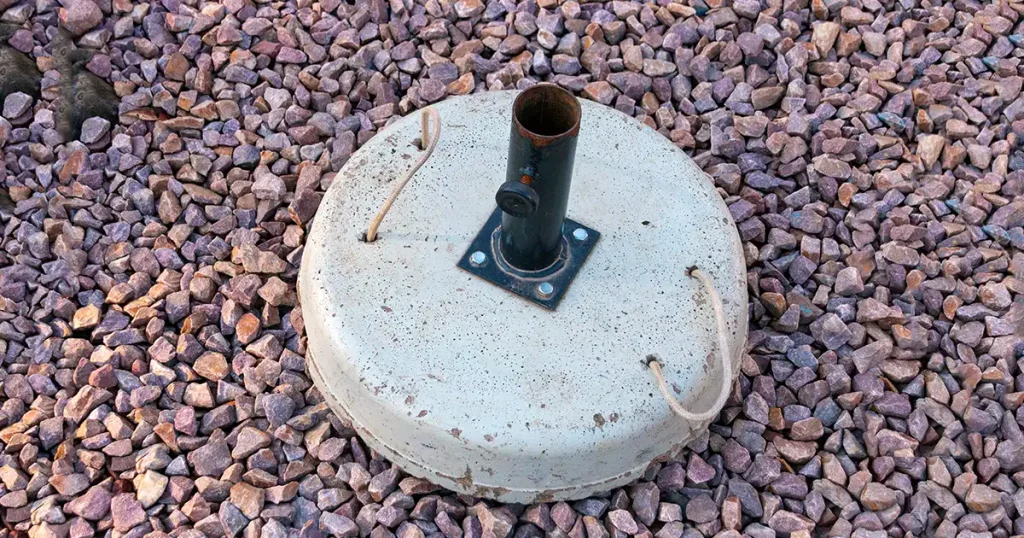 A concrete umbrella stand ontop of small stones in the garden