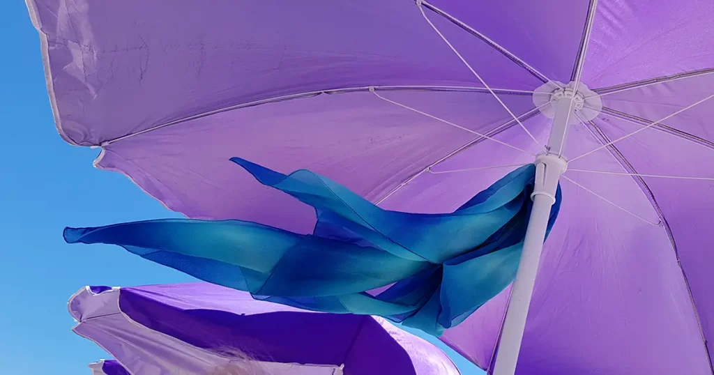 Wavy blue textile scarf under violet parasol on blue sky background