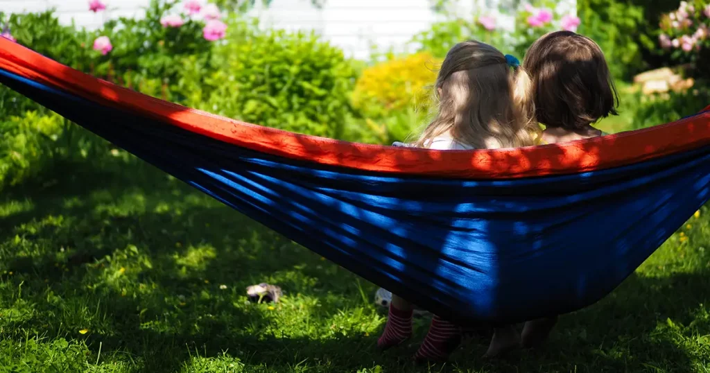 two little girls sitting in hammock in summer in garden rear view
