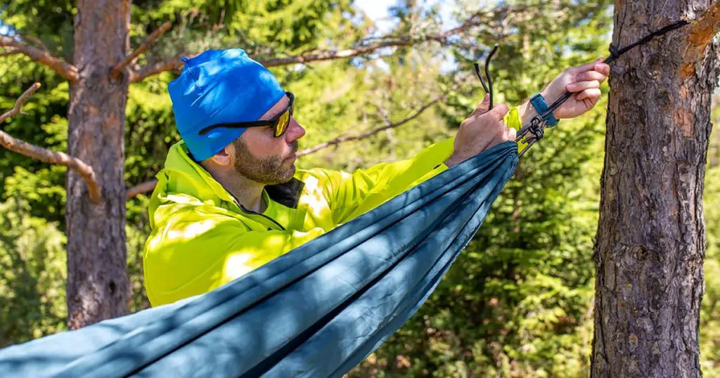 Man is setting up a hammock between two trees in the mountain.