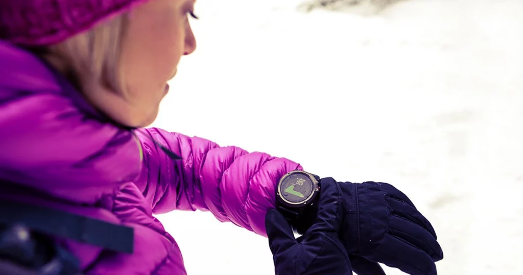 Woman hiker checking the elevation on sports watch, smartwatch with altimeter app in winter woods and mountains