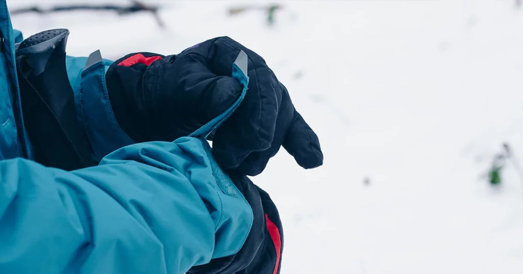 Hiker's hands in gloves are adjusting membrane jacket in the winter forest