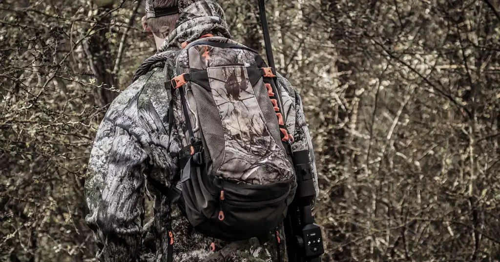 hunter in a camouflage suit with a backpack over his shoulders hunts in the forest, close-up, soft focus