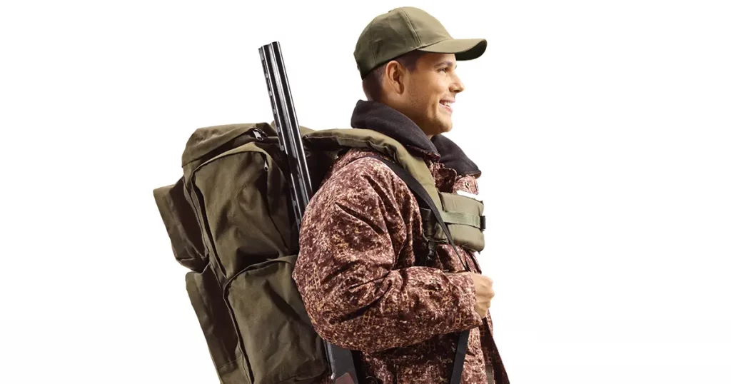 Hunter in a camouflage uniform standing with a backpack and shotgun isolated on white background