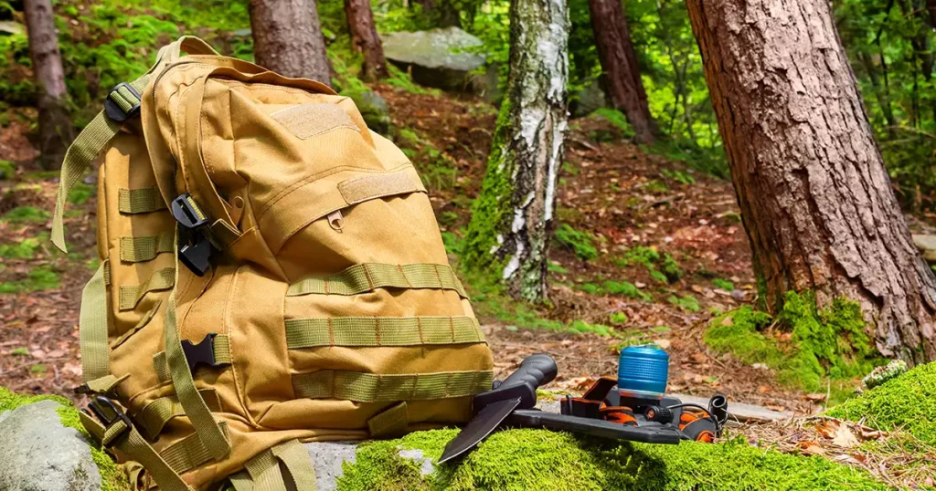 Photo of a tactical olive backpack laying with flashlight and hunting knife on daylight forest rocks with moss