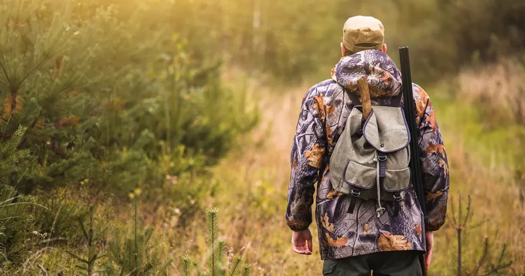 Hunter with a backpack and a hunting gun in the autumn forest.