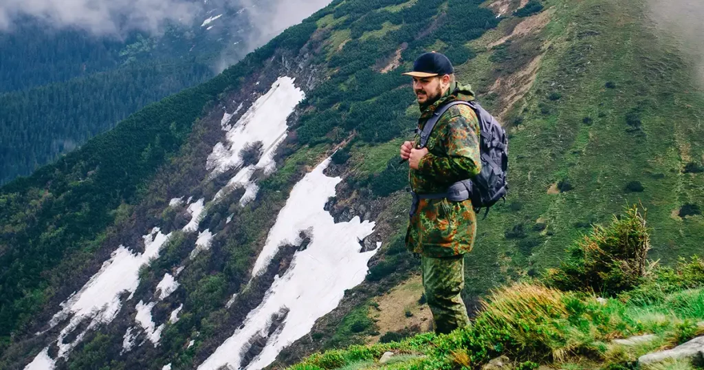 A young man in camouflage and a backpack in the mountains