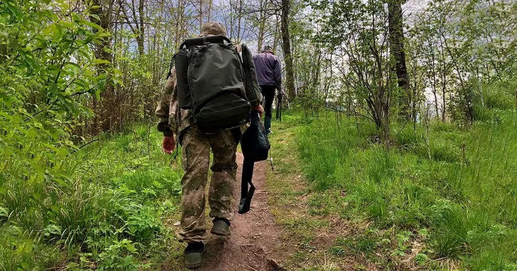 Fishermen lift with backpacks and fishing rods, return home after fishing.