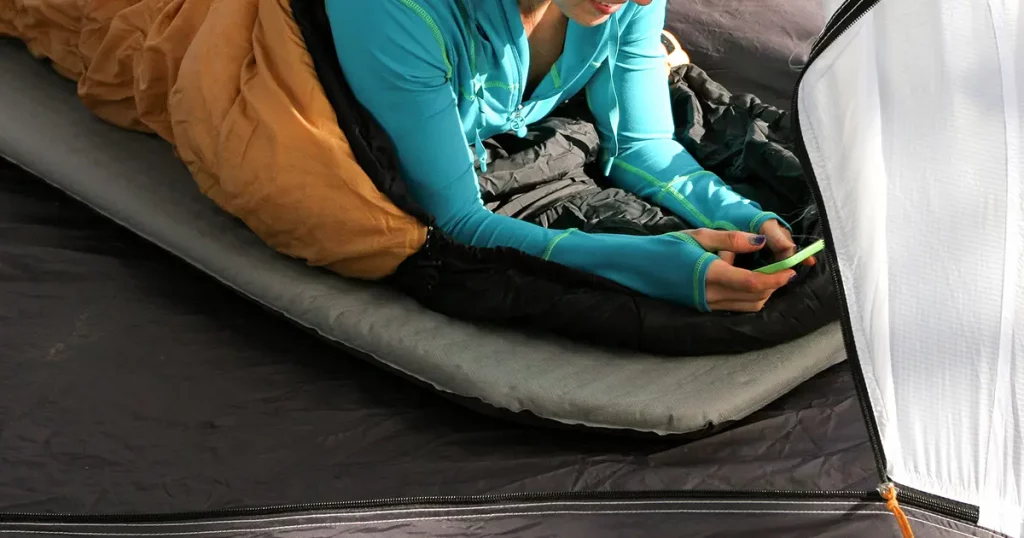 A woman on her phone while in her tent and sleeping bag